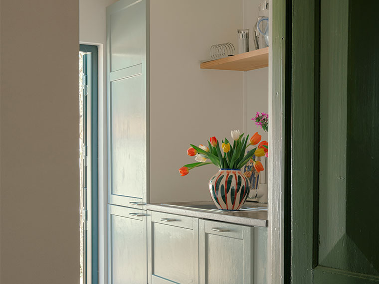 Vase med farverige tulipaner på køkkenbord ved grøn dørkarm.