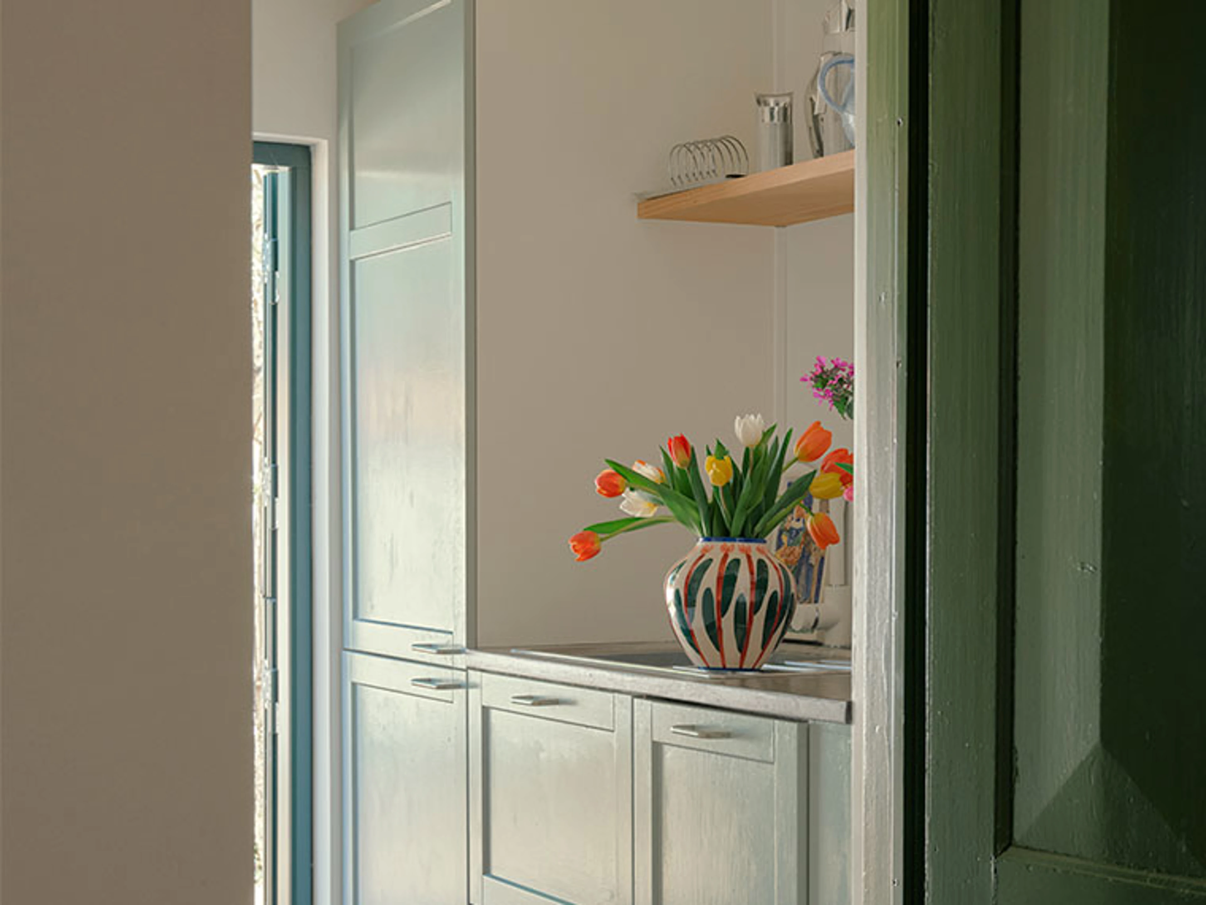 Vase med farverige tulipaner på køkkenbord ved grøn dørkarm.