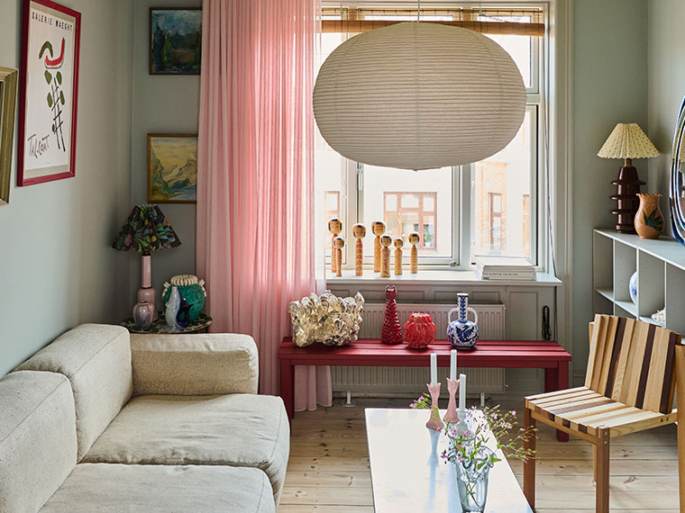 Farverig stue med lyserøde gardiner, hvid sofa, rød bænk under vinduet og dekorative kunstgenstande.