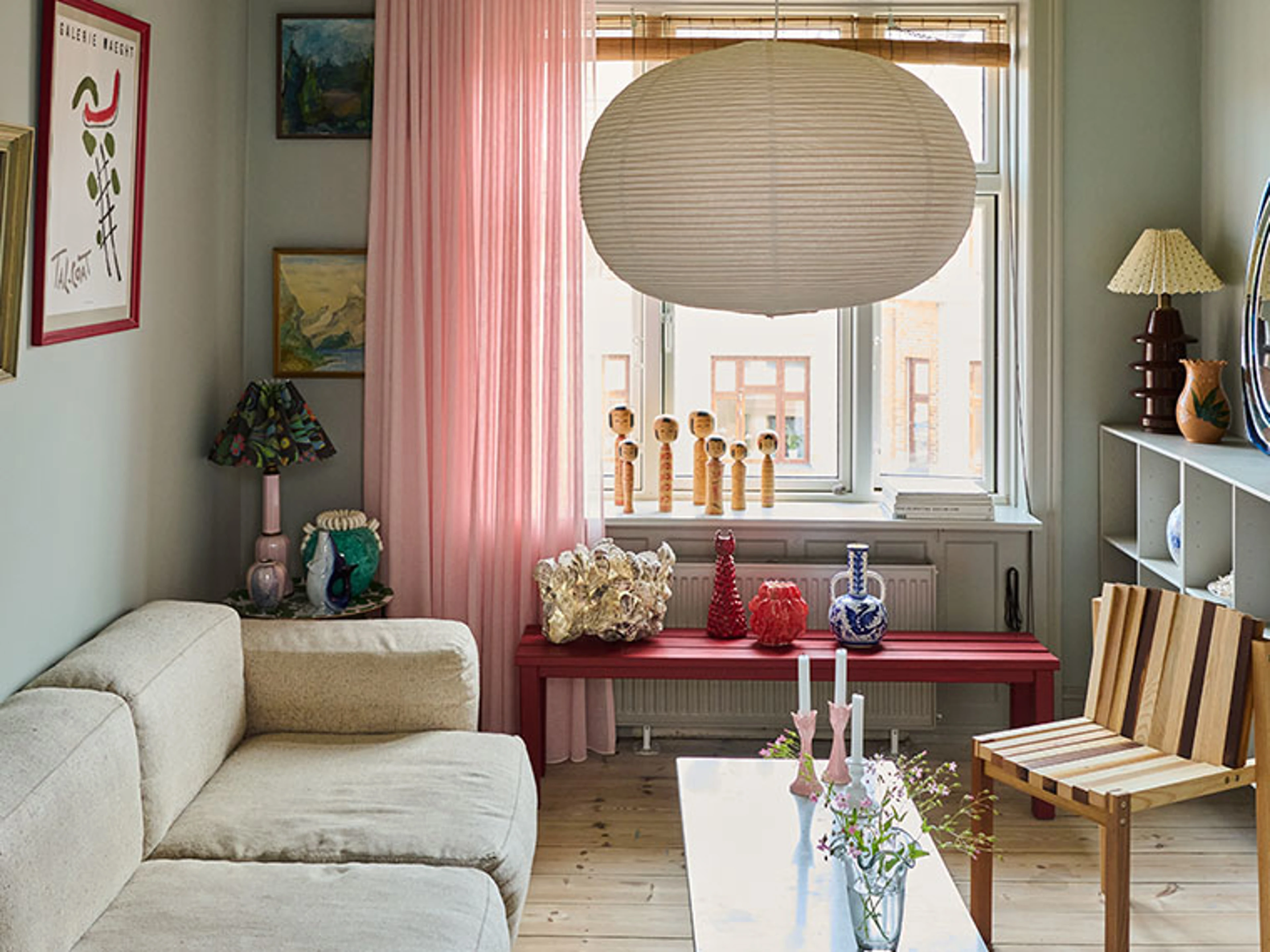 Farverig stue med lyserøde gardiner, hvid sofa, rød bænk under vinduet og dekorative kunstgenstande.