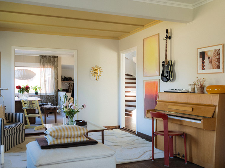 Living room with yellow-painted ceiling beams, a piano and an electric guitar on the wall.