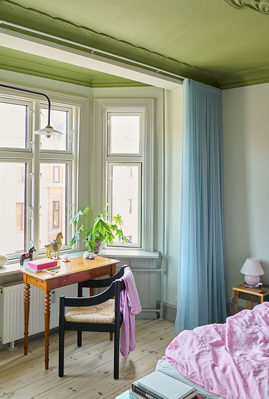 Soveværelse med grønt loft, skrivebord ved vindue og lyseblå gardiner.