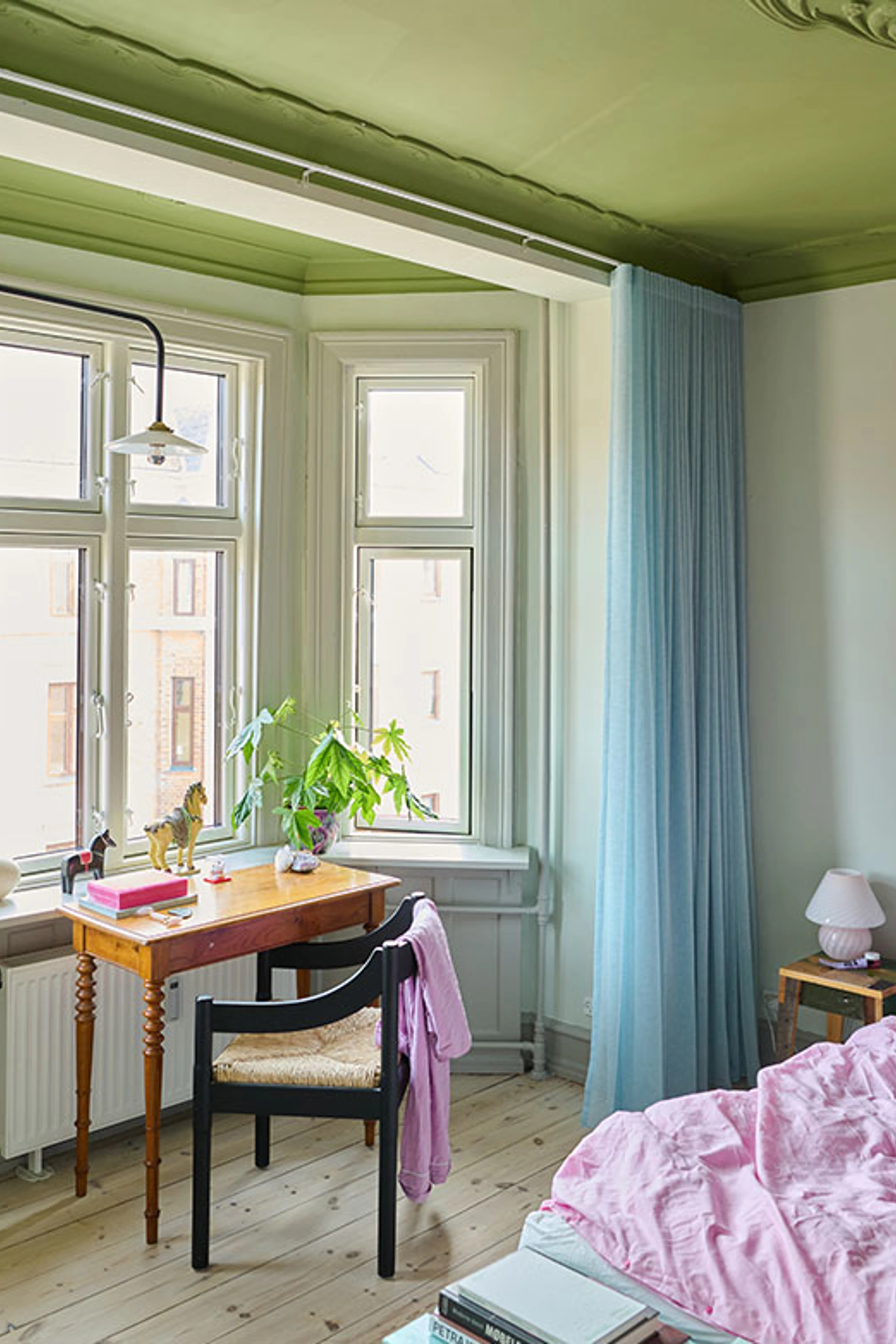 Soveværelse med grønt loft, skrivebord ved vindue og lyseblå gardiner.