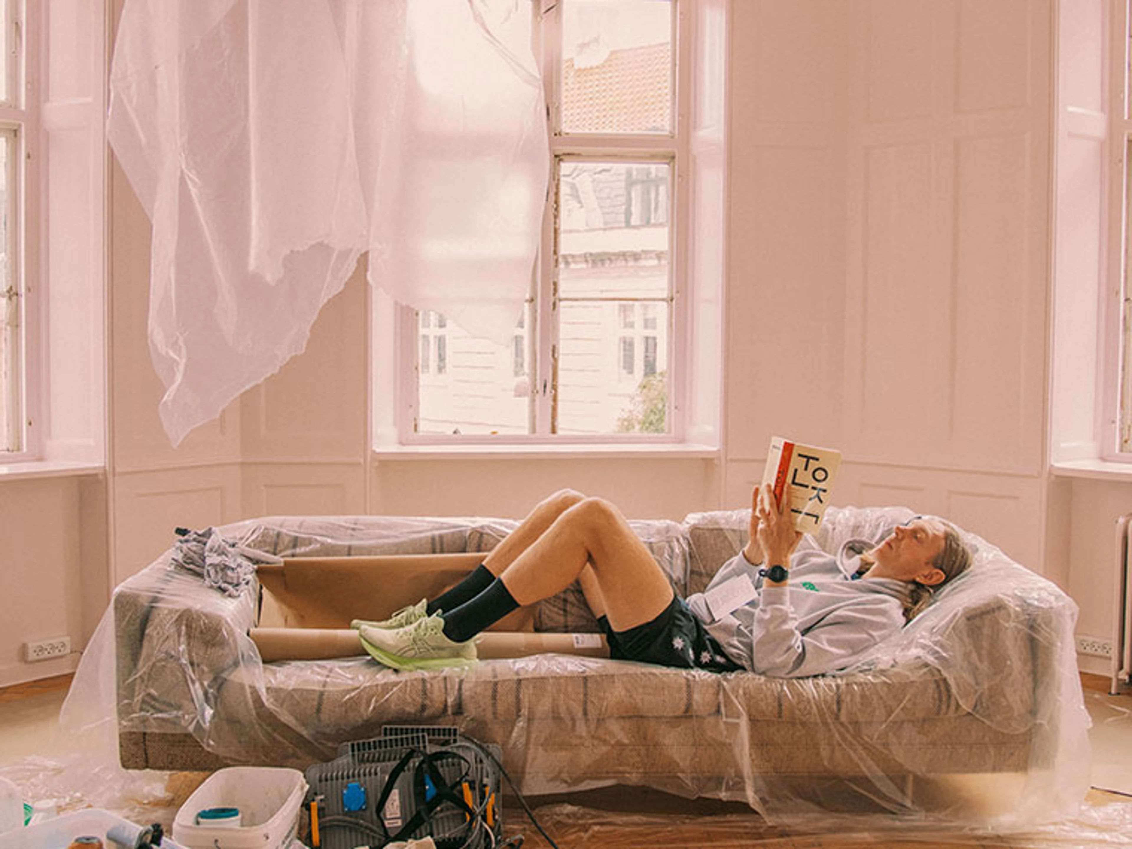 Person læser på en sofa dækket med plastik.