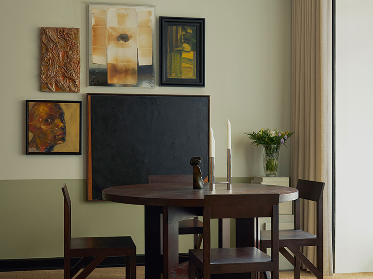 Round dining table with dark wood chairs in front of a gallery wall featuring abstract paintings in earthy tones.