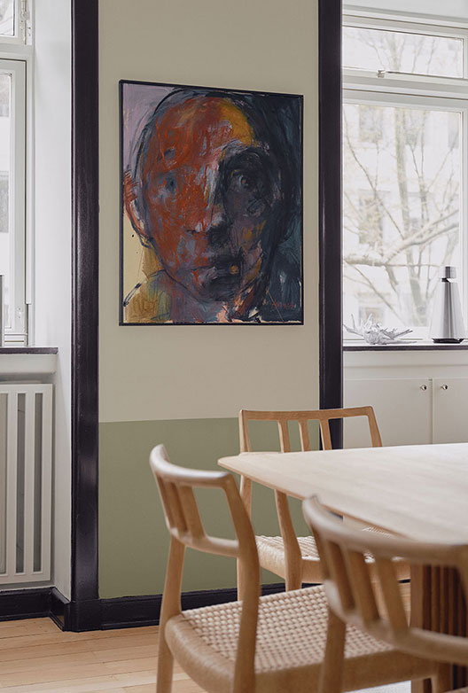 Væg i 2 grønlige nuancer i spisestuen med et abstrakt maleri af et ansigt i midten, omringet af sorte paneler.