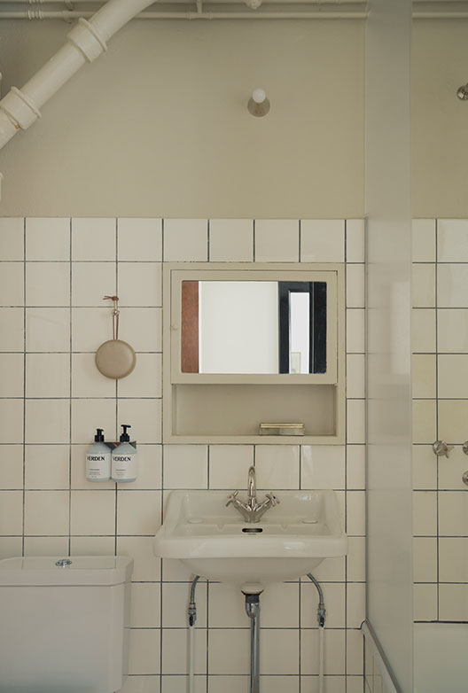 Bright bathroom with white square tiles, a classic sink, mirrored cabinet, and exposed pipes.