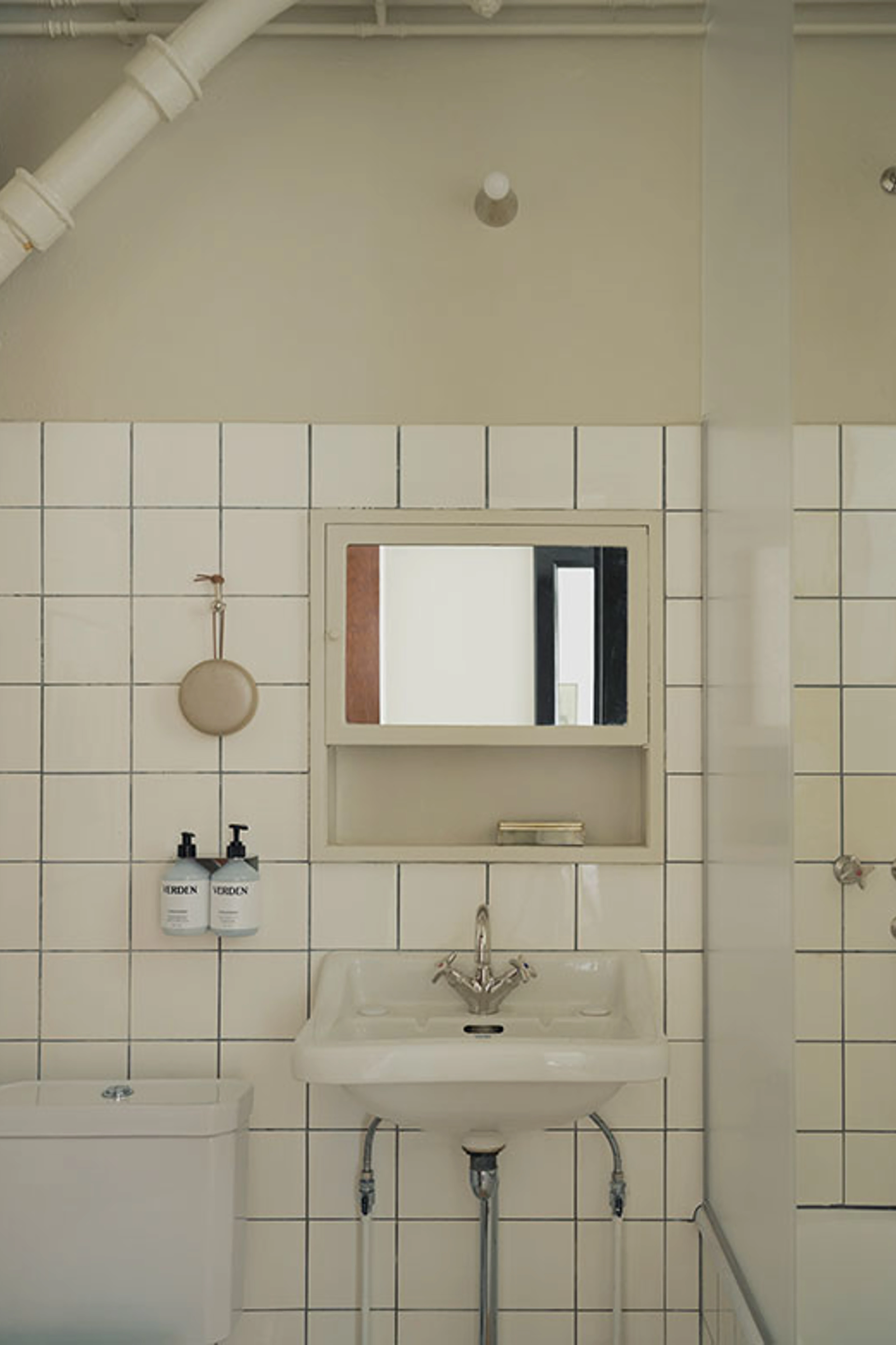 Bright bathroom with white square tiles, a classic sink, mirrored cabinet, and exposed pipes.