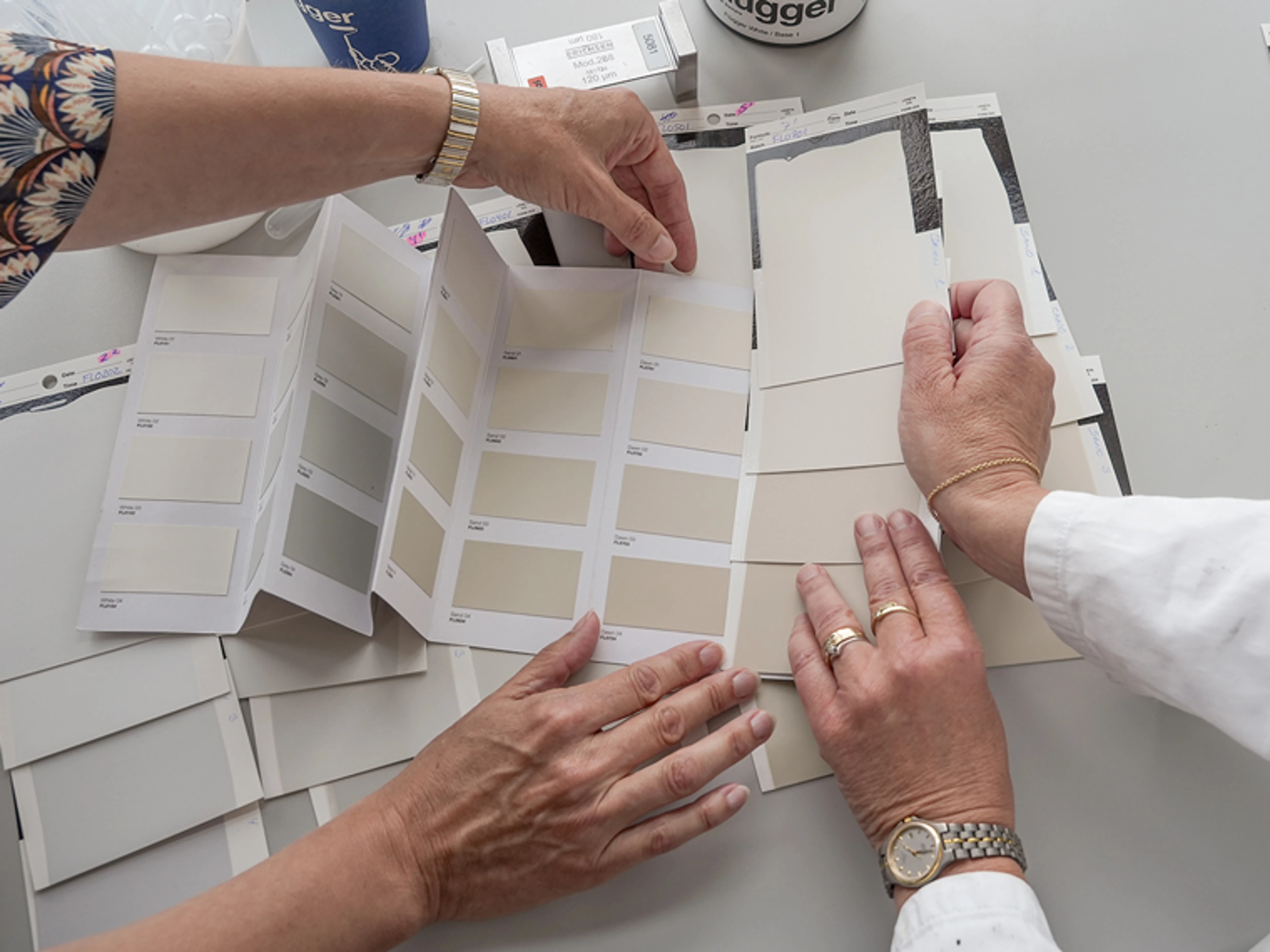 Two people comparing Flügger 32 colour cards and paint samples in neutral beige and grey shades.