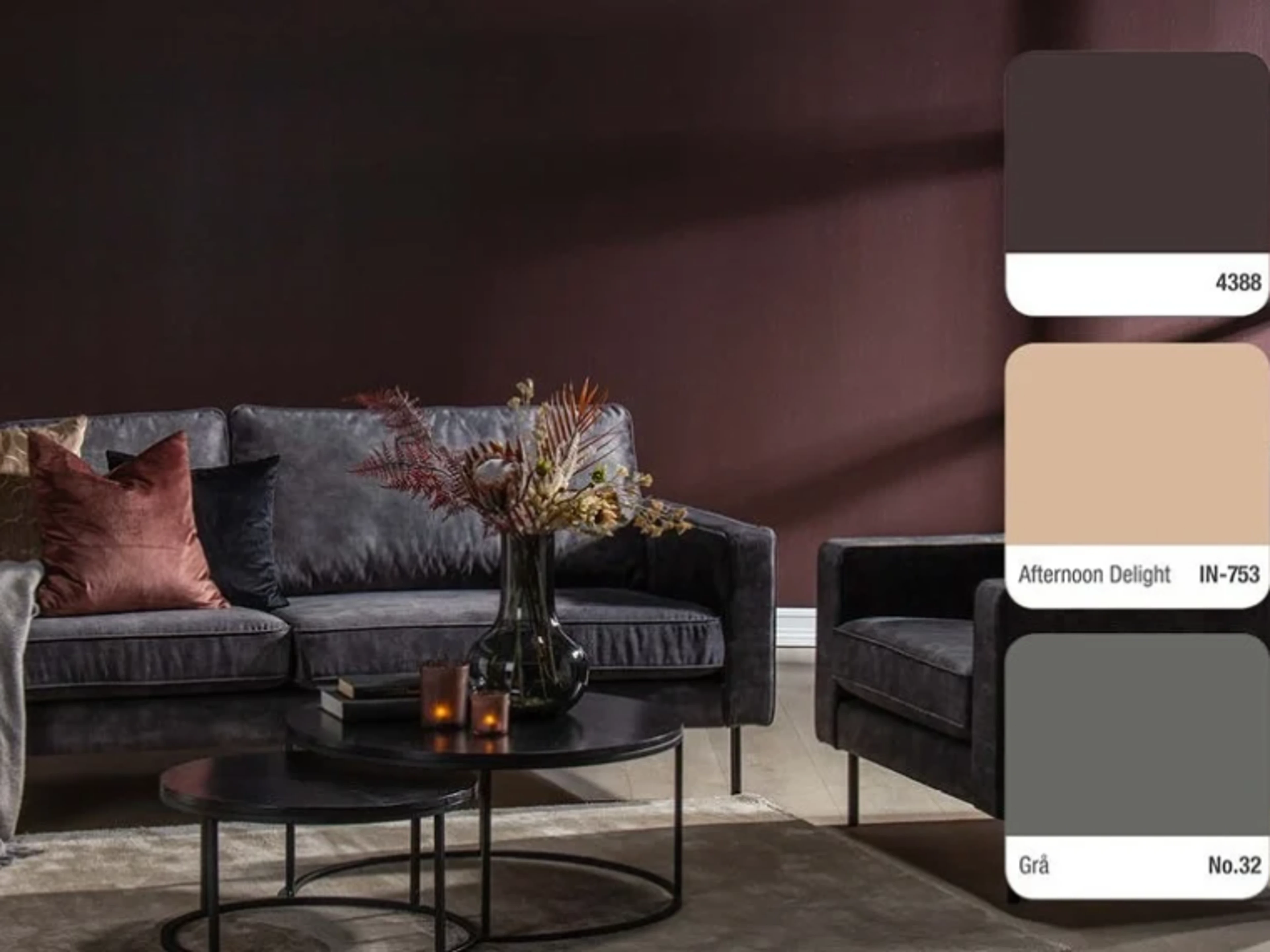 Living room with dark burgundy walls, a dark grey sofa and armchair, round black coffee tables and a vase with dried flowers, with three colour swatches on the right: 4388, Afternoon Delight IN-753 and Grå No.32.