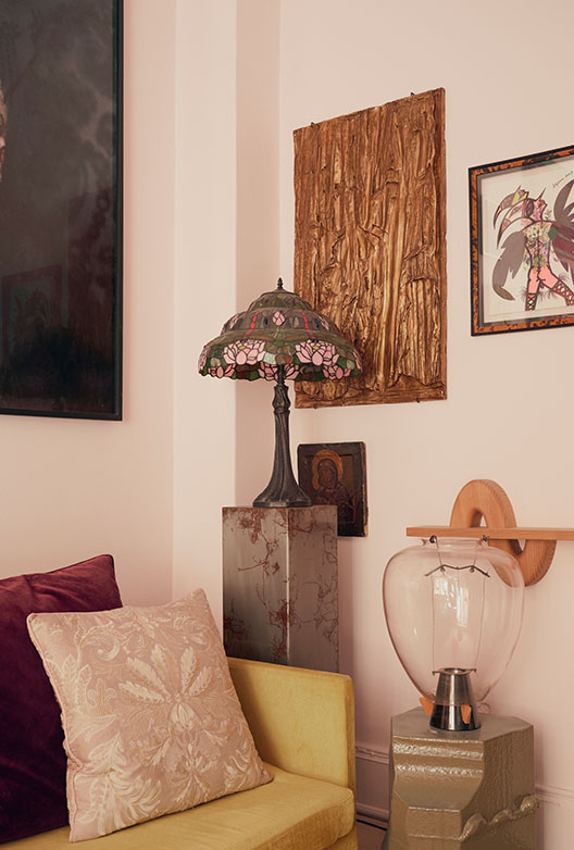 Detalje fra stue med gul sofa, dekorativ bordlampe og en samling forskellige kunstværker på væggen.