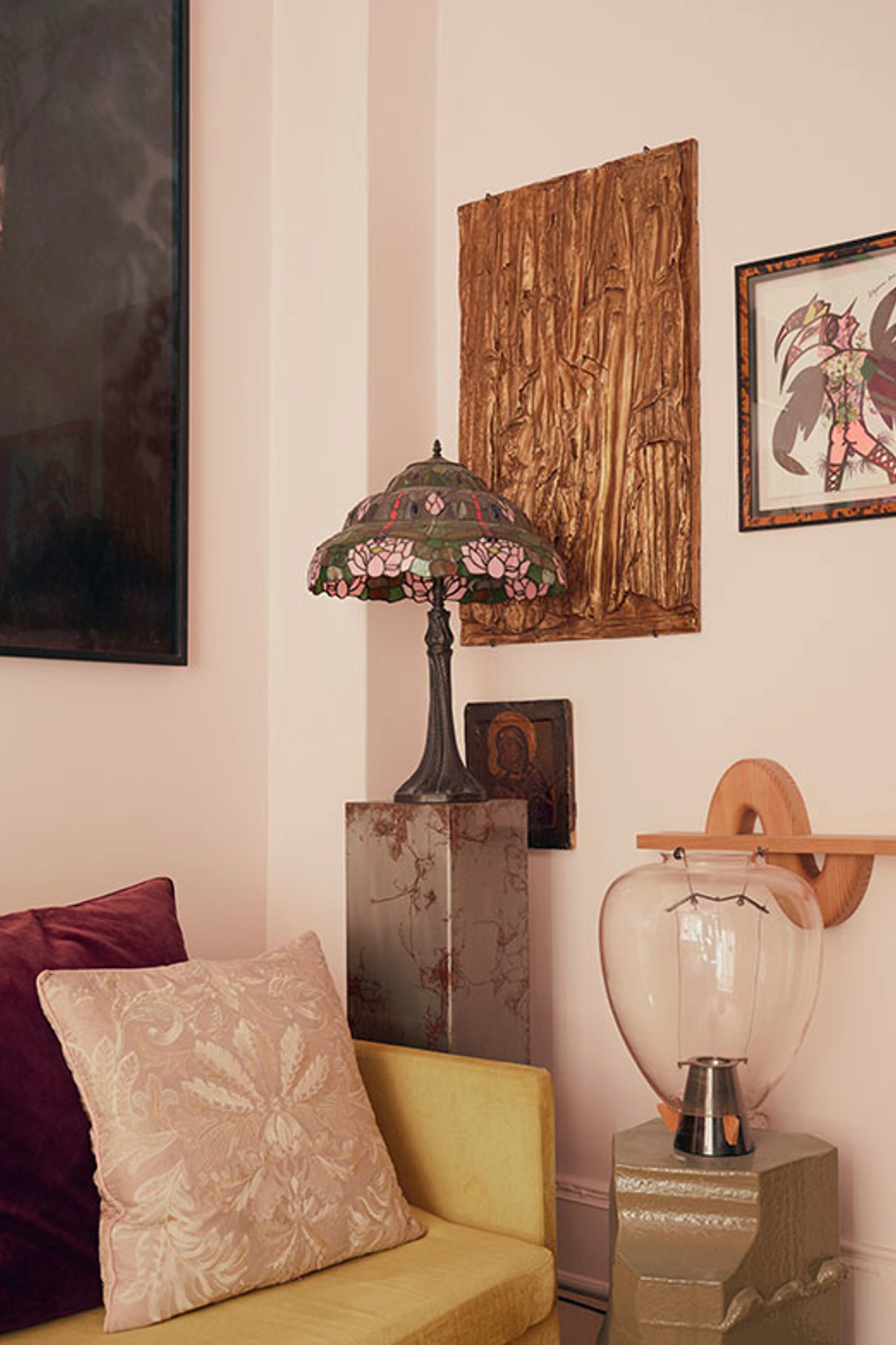 Detalje fra stue med gul sofa, dekorativ bordlampe og en samling forskellige kunstværker på væggen.