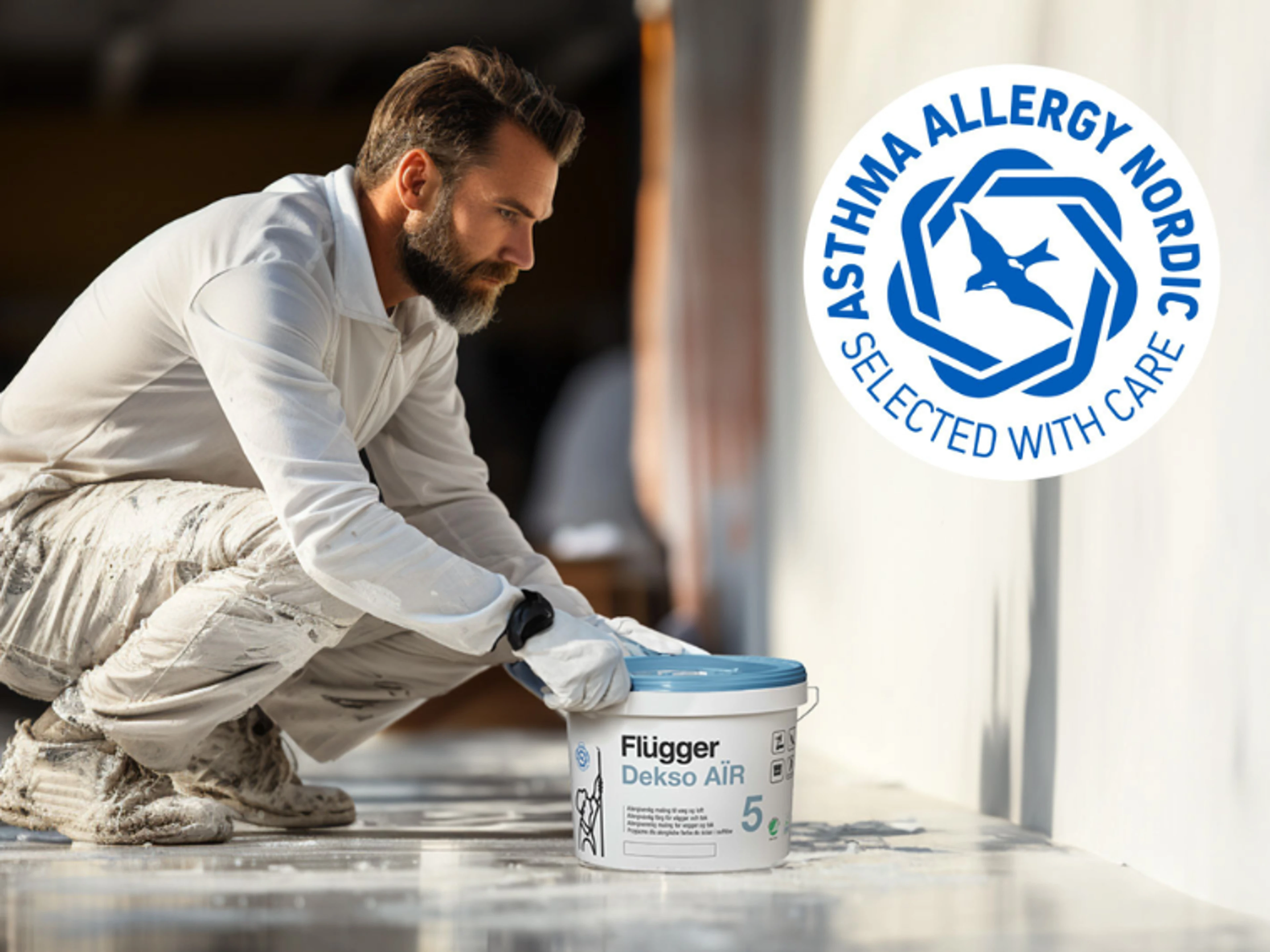 Person by a wall with a bucket of Flügger Dekso Air paint, with the Asthma Allergy Nordic label visible in the image.