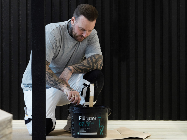 Professionel maler maler træstolp med Wood Tex 07 maling med pensel i sort farve.