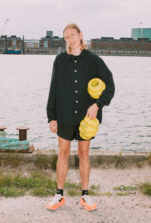 Person står ved vandet med gule vaser.