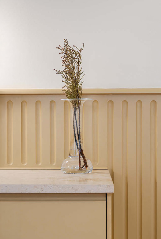 Beige panelvegg med glassvase og tørkede grener på et lyst skap.