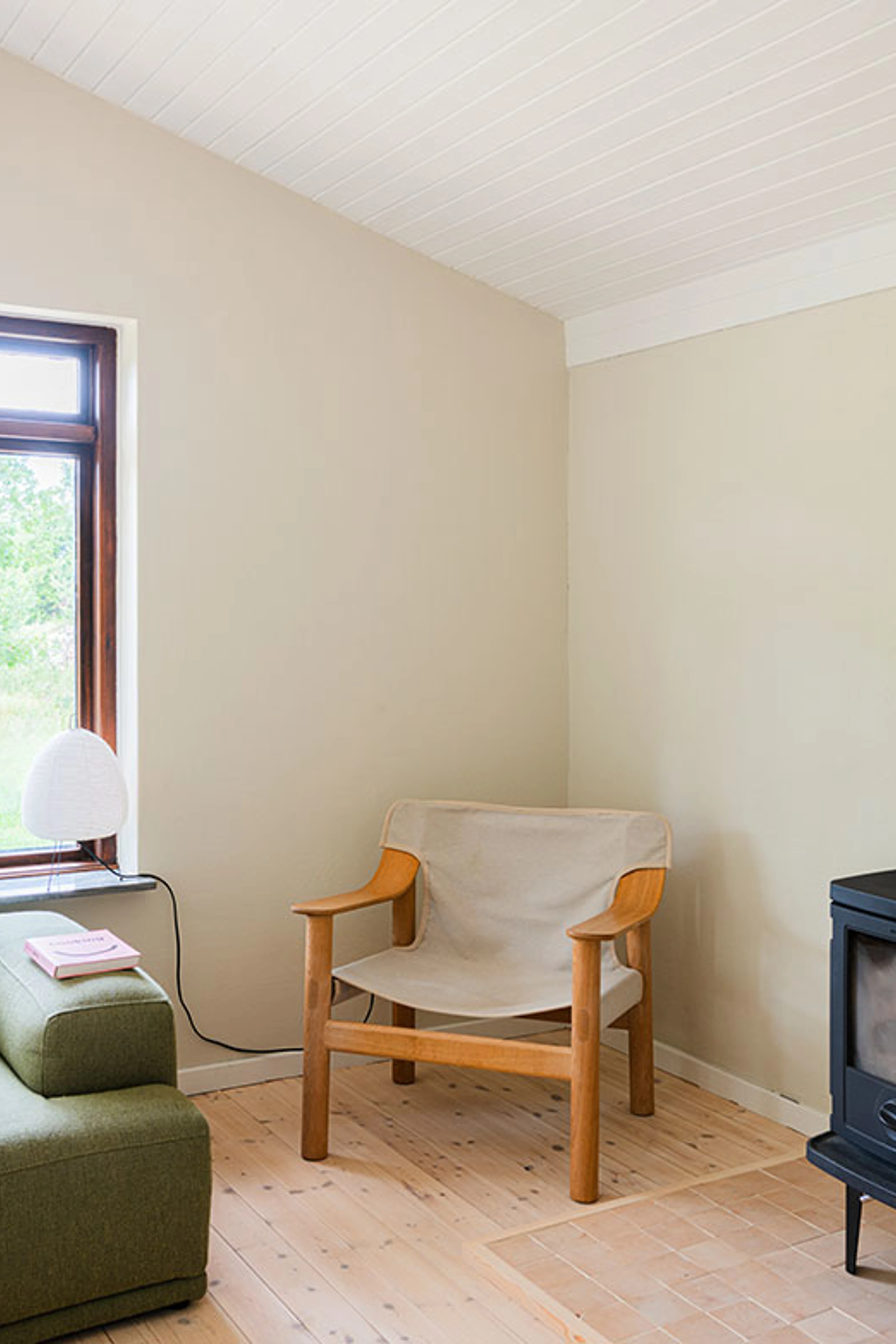 Living room corner with beige walls, a white ceiling and a wooden armchair next to a green sofa.