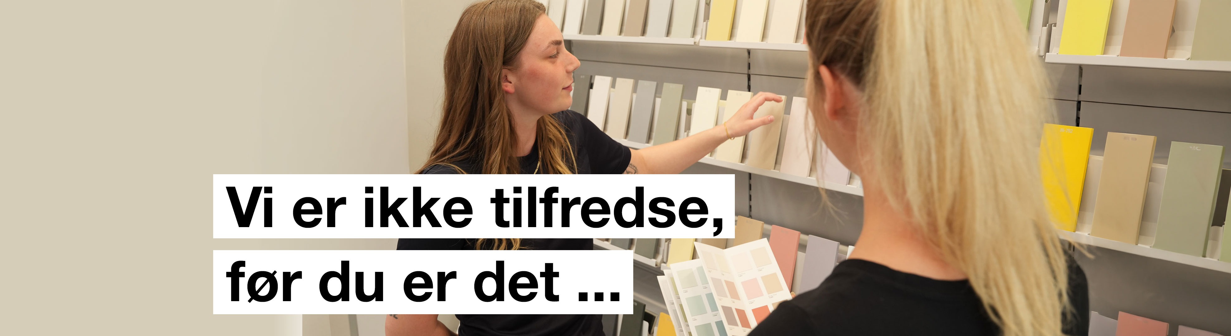 Banner med to personer der ser på farvekort med teksten "Vi er ikke tilfredse før du er det..." skrevet på.