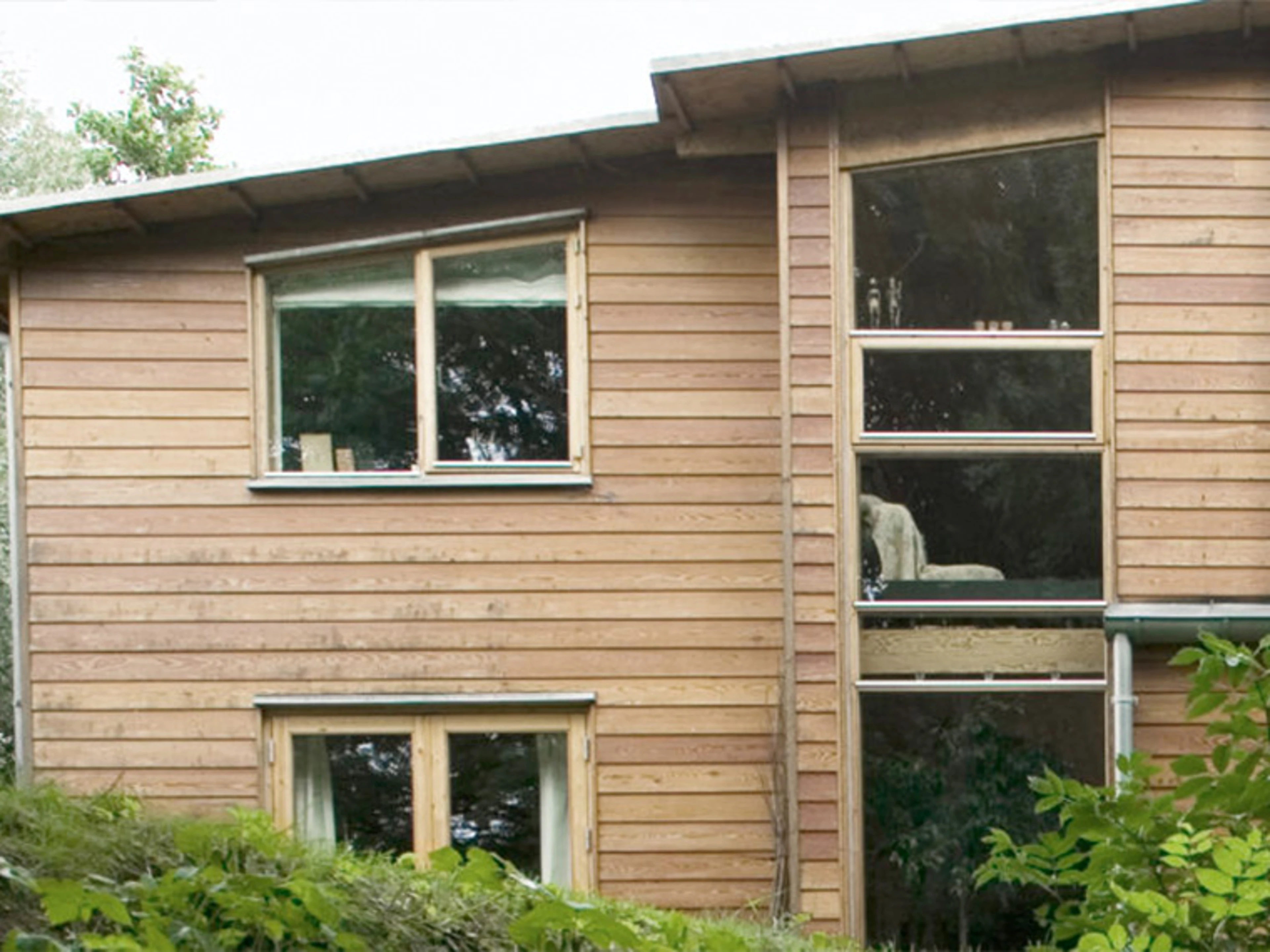 Modern house with a natural wood façade surrounded by trees and greenery.