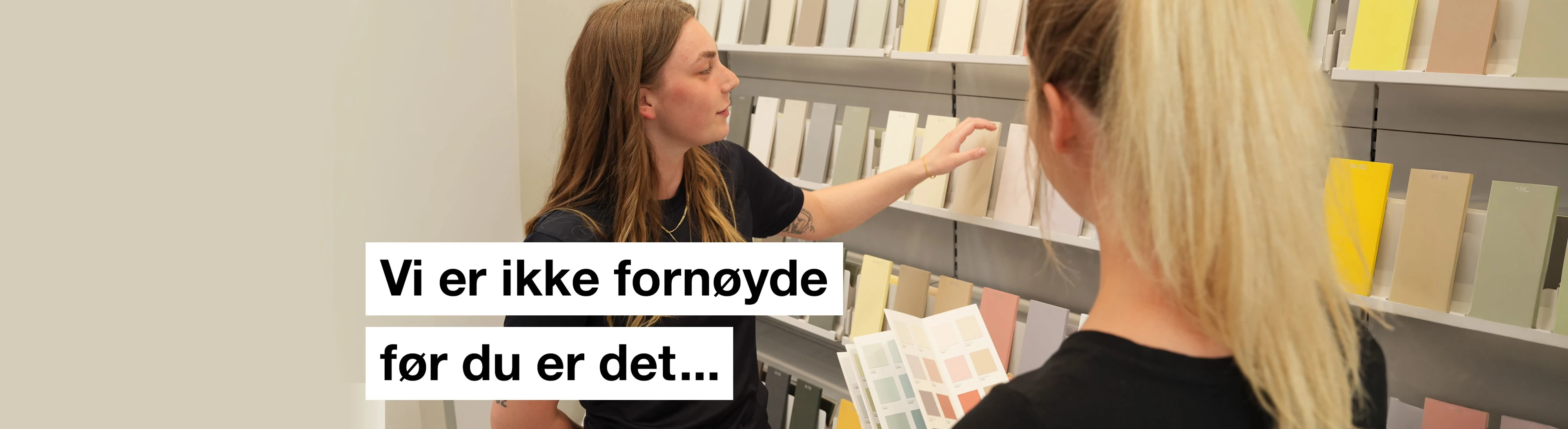 Banner med to personer der ser på farvekort med teksten "Vi er ikke fornøyde før du er det..." skrevet på.
