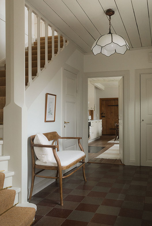 Entré med trappe, lænestol, loftlampe og dør til køkken.