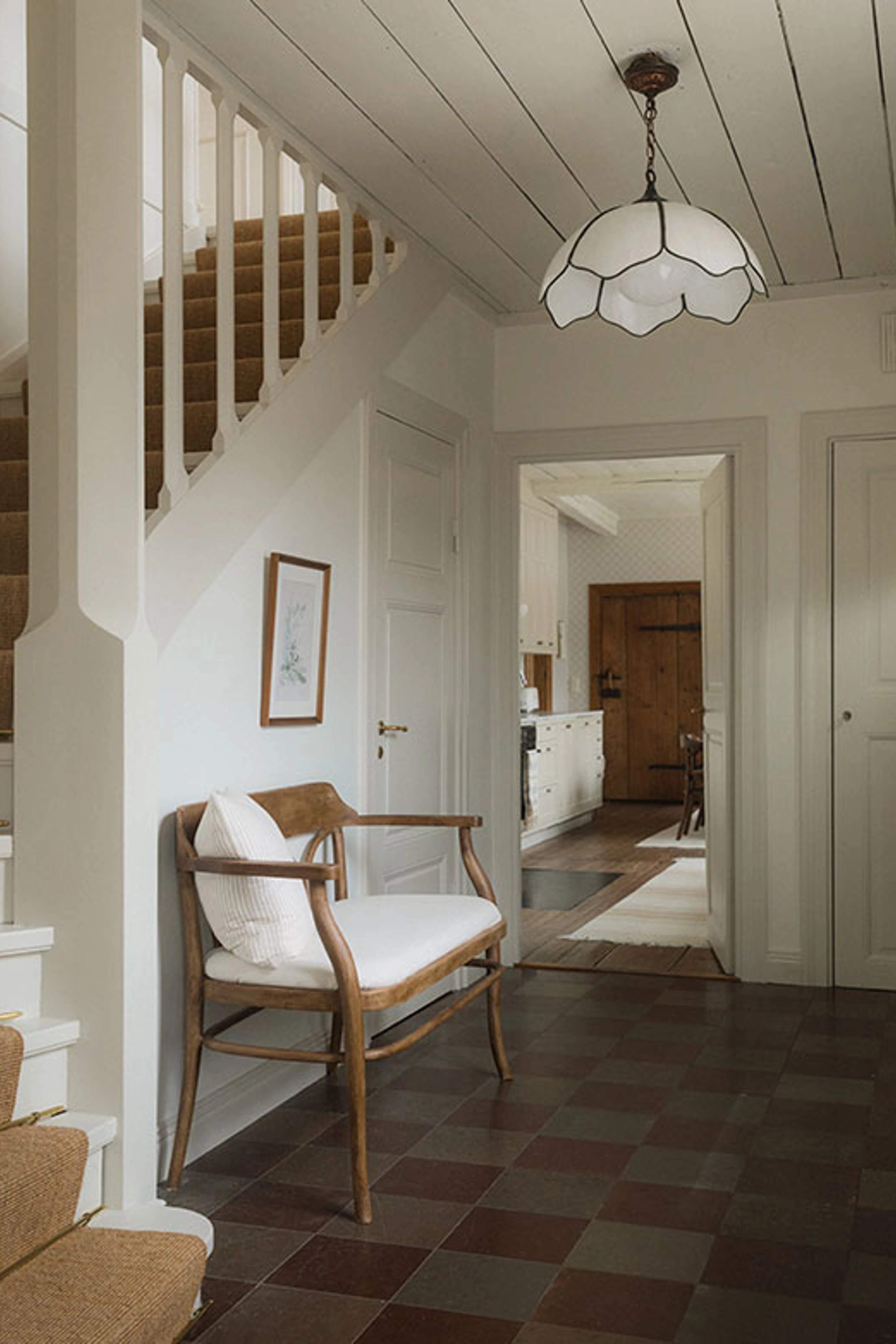 Entré med trappe, lænestol, loftlampe og dør til køkken.