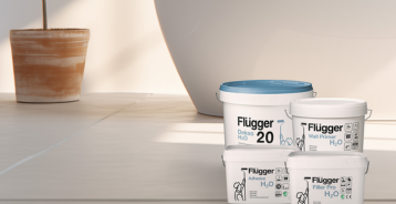 Spande med Flügger H2O-serie står på et lyst gulv foran en lysmalet væg i en blød greige nuance.
