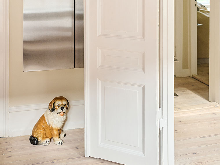 Lille keramisk hundefigur ved åben hvid dør i lys entré.