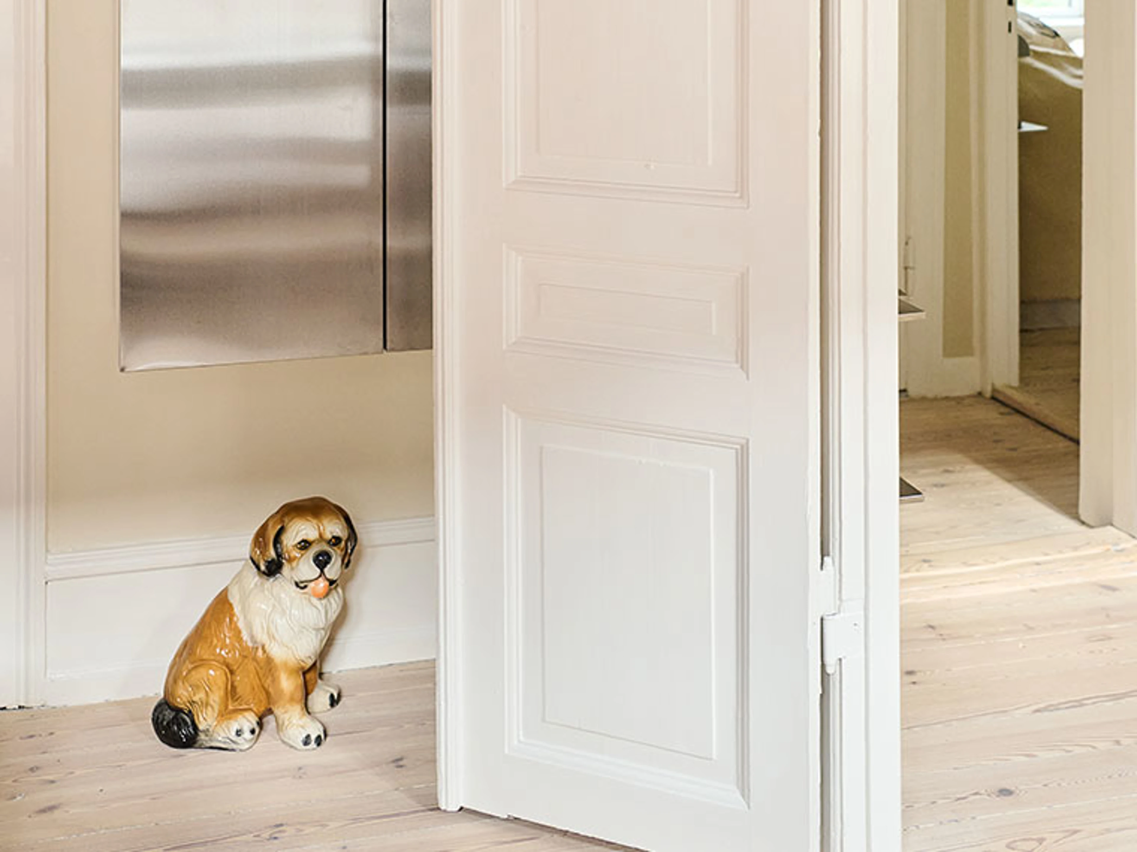 Lille keramisk hundefigur ved åben hvid dør i lys entré.