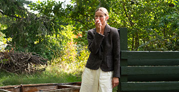 Woman eats an apple in the garden by a dark green fence.