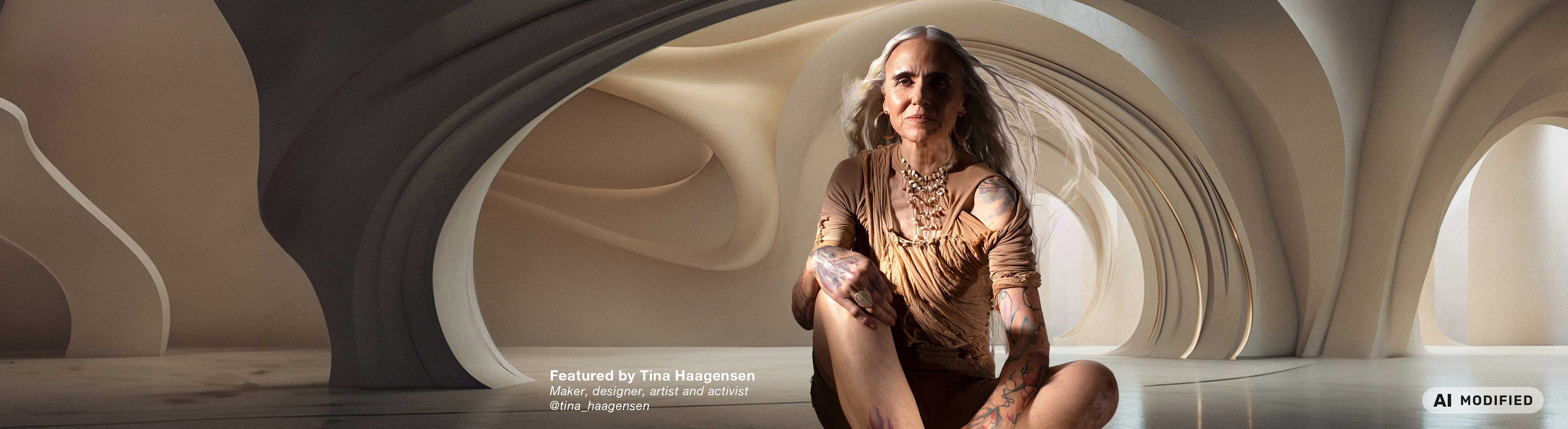 Person med langt gråt hår og synlige tatoveringer sidder i et arkitektonisk miljø med organiske, bølgende former i varme beige og sandfarvede nuancer. Tøjets farver og omgivelserne er inspireret af Flügger-farven Cotton (FL8012).