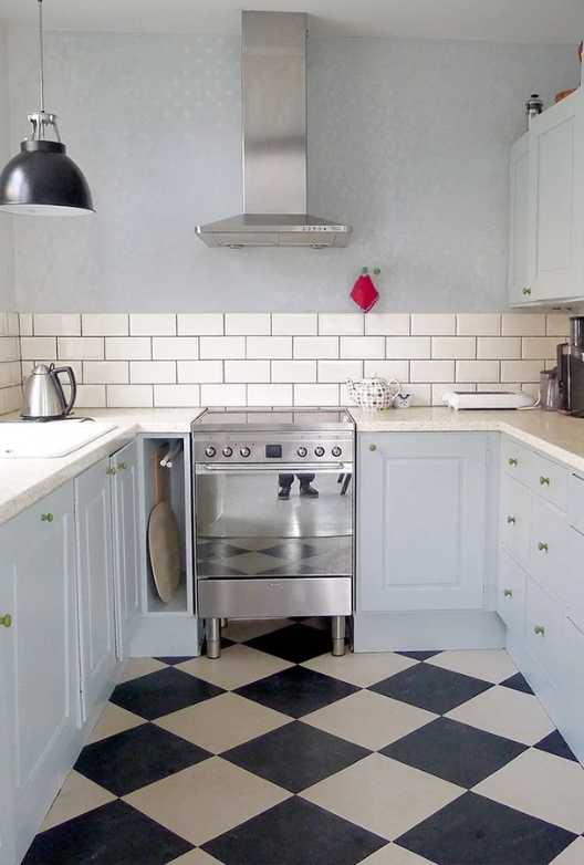Traditional kitchen with light blue cabinets, white wall tiles, a stainless steel cooker and black-and-white chequered floor.