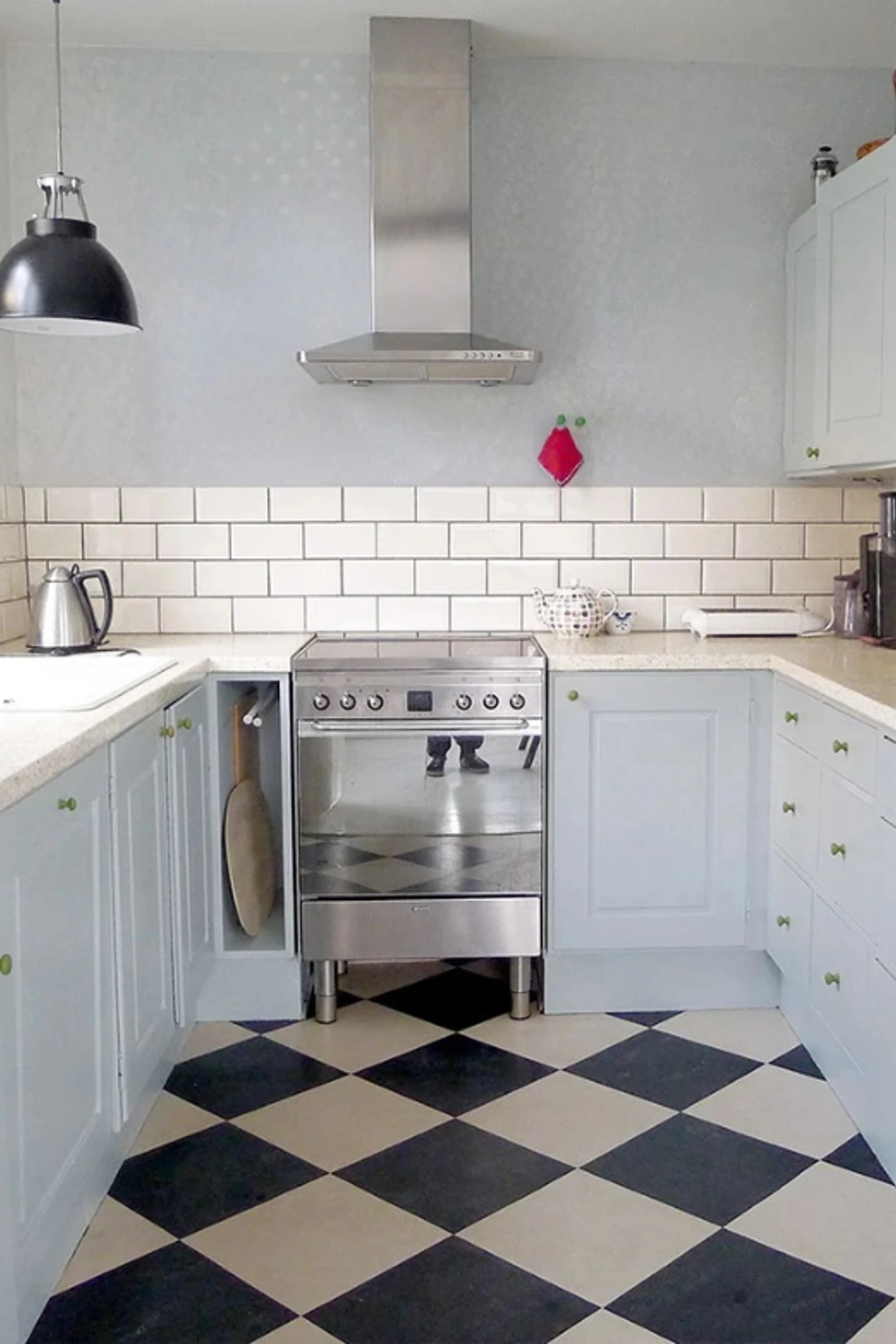Traditional kitchen with light blue cabinets, white wall tiles, a stainless steel cooker and black-and-white chequered floor.