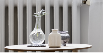 Lite bord med dekorative vaser i glass og keramikk plassert foran en hvit radiator.