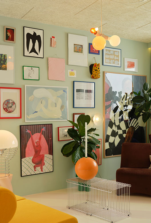 Living room with mint green walls, a dense gallery wall, large green plants, and colorful sculptural lamps.