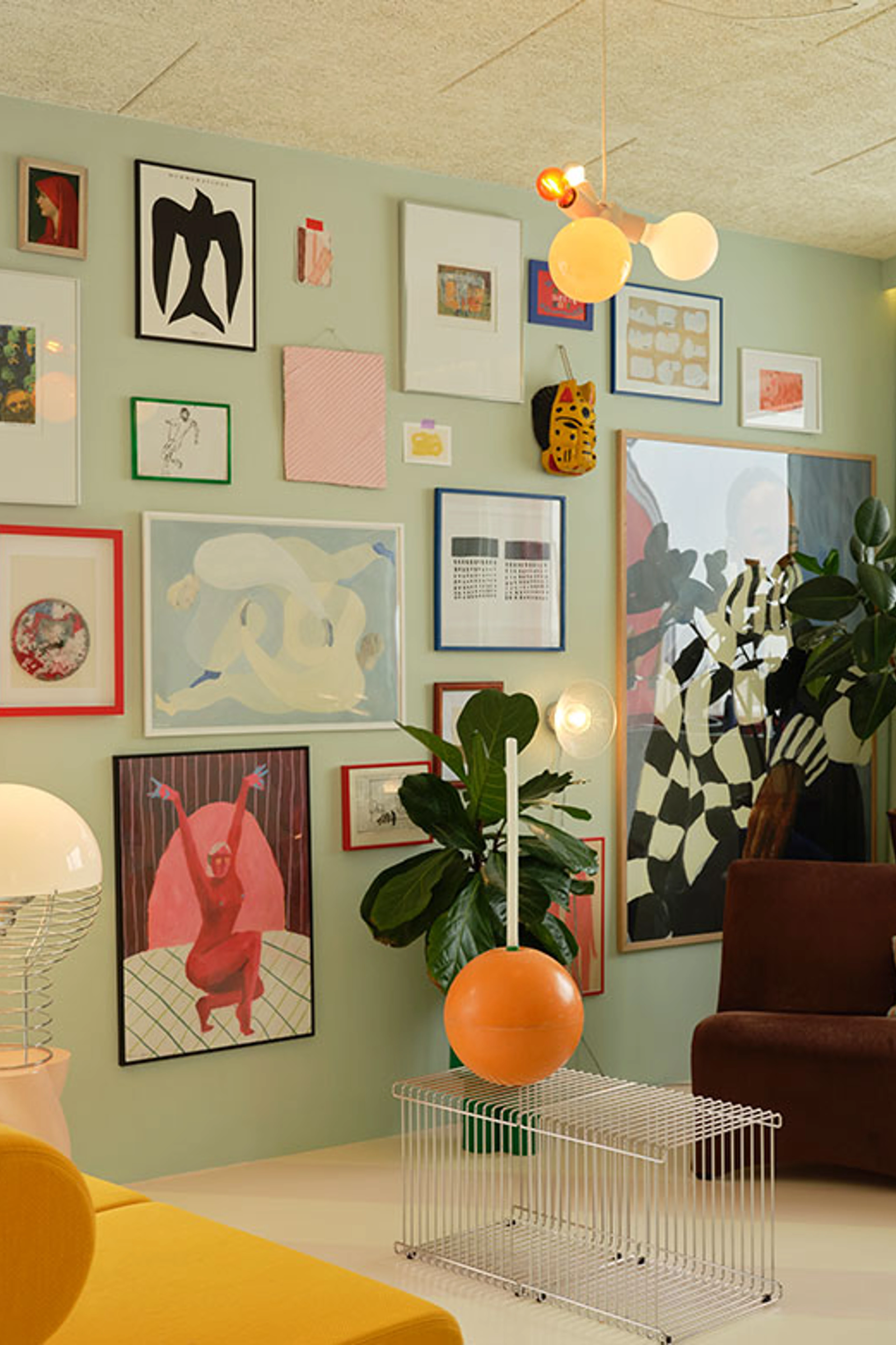 Living room with mint green walls, a dense gallery wall, large green plants, and colorful sculptural lamps.