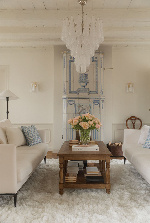 Stue med hvide sofaer, lysekrone og sofabord med blomster.