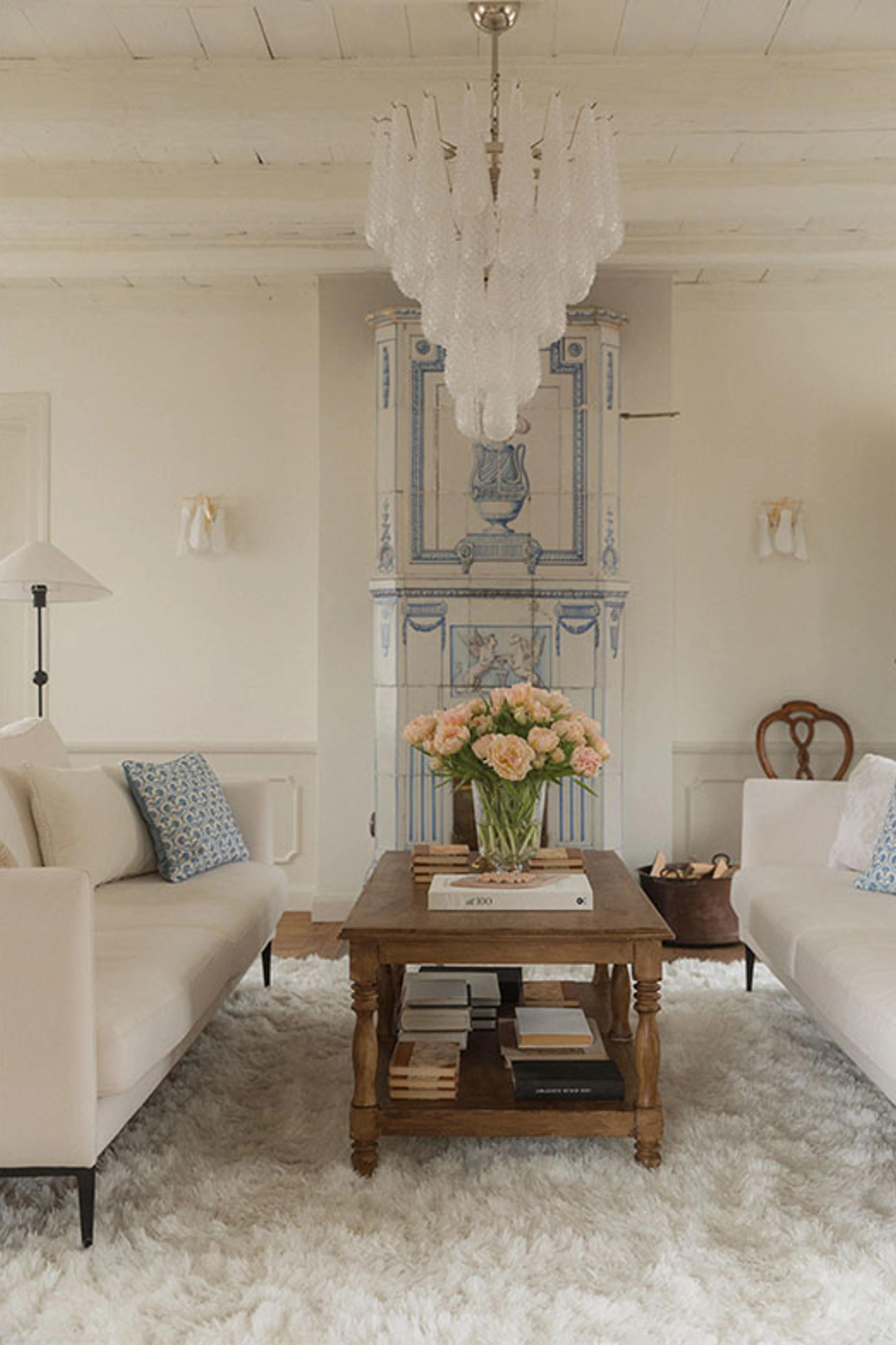 Stue med hvide sofaer, lysekrone og sofabord med blomster.