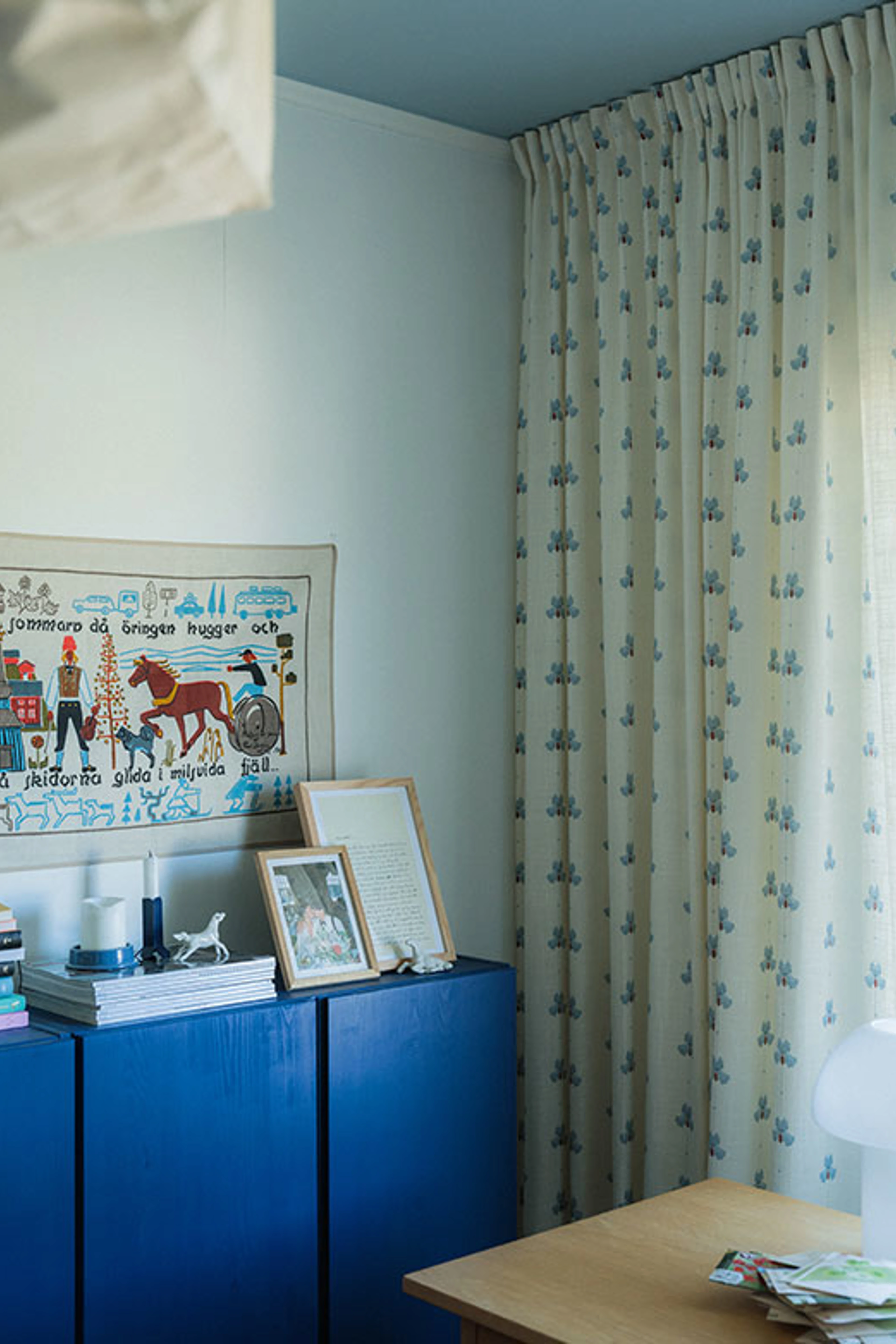 Room with light blue walls, a cobalt blue cabinet and floral-patterned curtains.