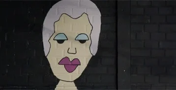 Illustrert ansikt av en person med grått hår, blå øyeskygge og lilla lepper, malt på en mørk murvegg.