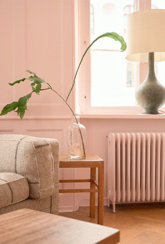 Grøn gren i vase foran rosa væg.