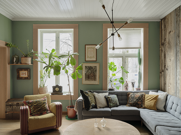 Grøn stue med store vinduer, mange planter, grå hjørnesofa og en sennepsgul vintage-lænestol.