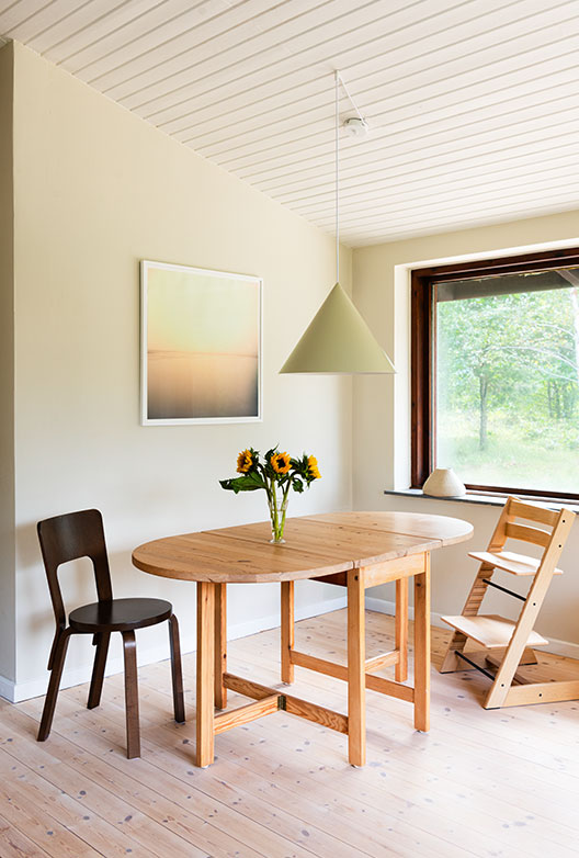 Dining area with light beige walls, a pine dining table with sunflowers and a green pendant lamp.