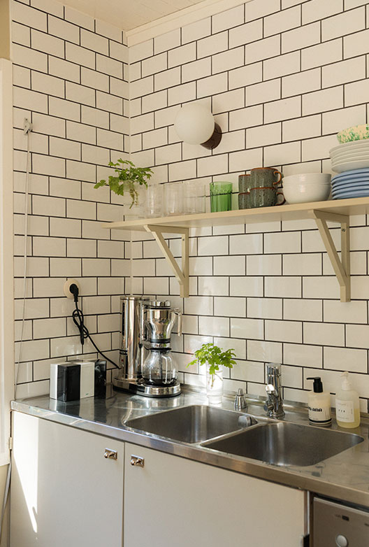 Kitchen with white subway tiles, a wooden shelf and a stainless steel sink.
