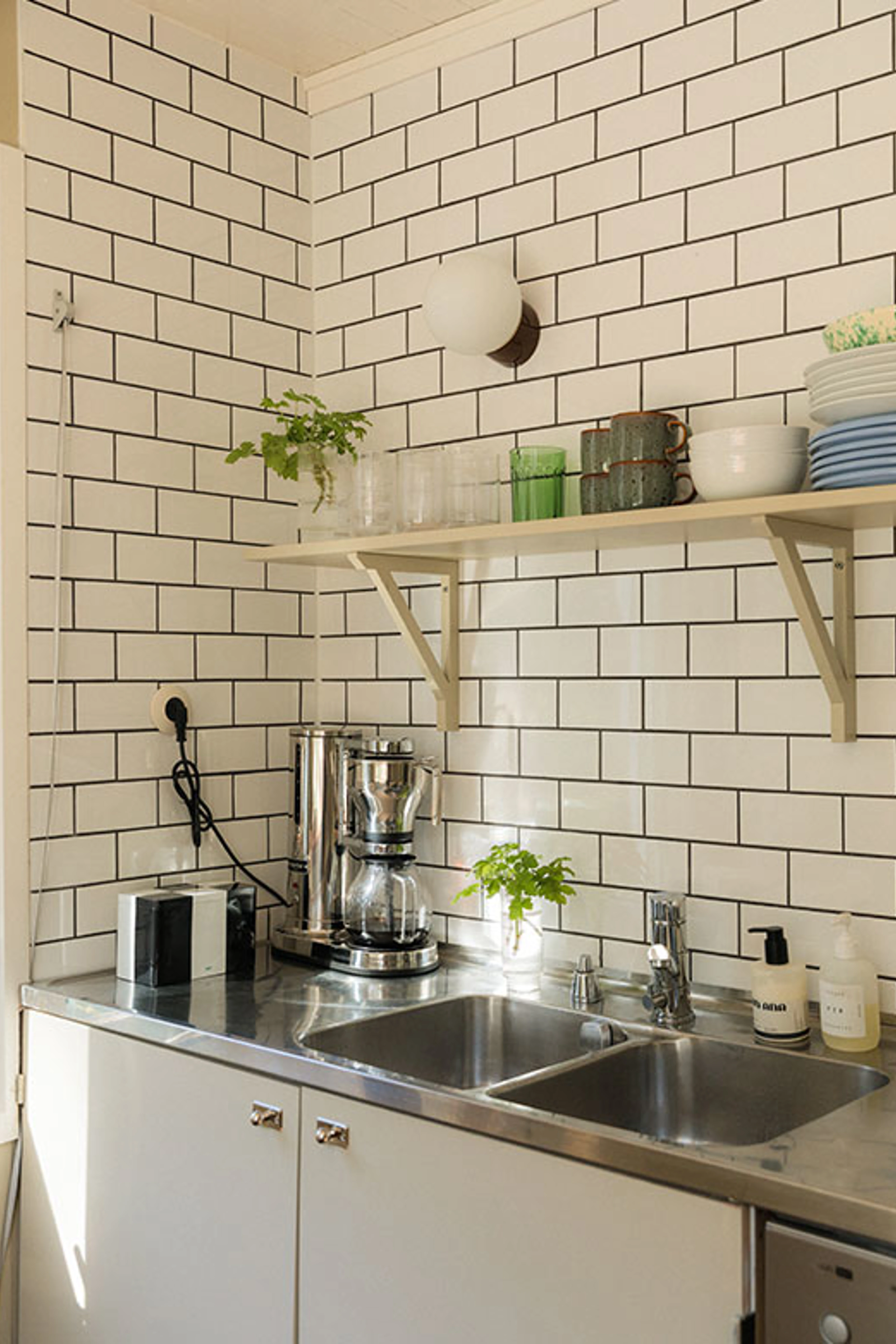 Kitchen with white subway tiles, a wooden shelf and a stainless steel sink.