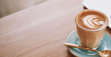 Træbord med en kop kaffe på en blå tallerken og en guldske.