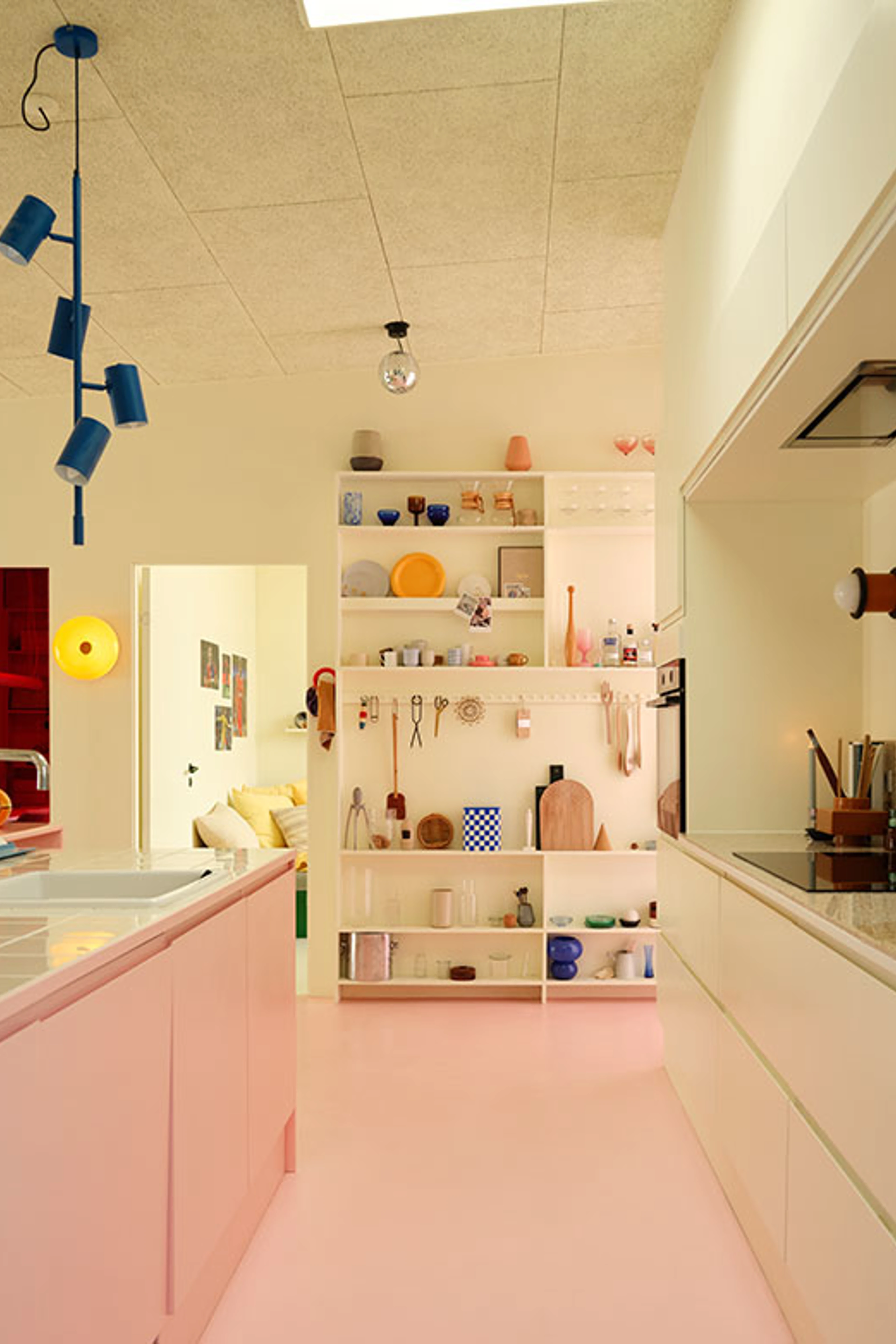 Colorful kitchen with a pink floor and kitchen island, light-colored cabinets, open shelving, and blue pendant lights.