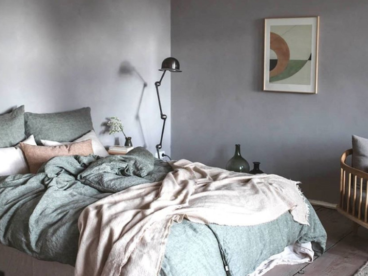 Soveværelse med vægge spartlet i grå, seng med grønne tekstiler og beige plaid, sort gulvlampe ved siden af sengen samt grafisk kunstværk på væggen.