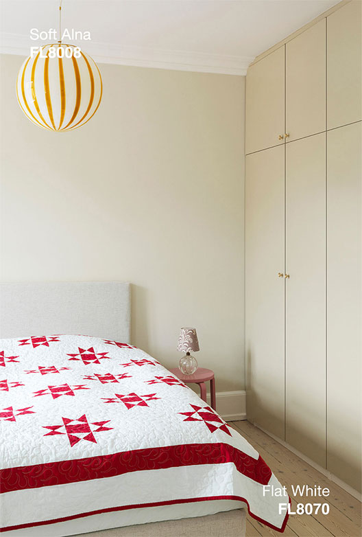 Lyst soveværelse med vægge i Soft Alna og indbyggede skabe i Flat White, indrettet med seng, mønstret sengetæppe og stribet loft lampe.