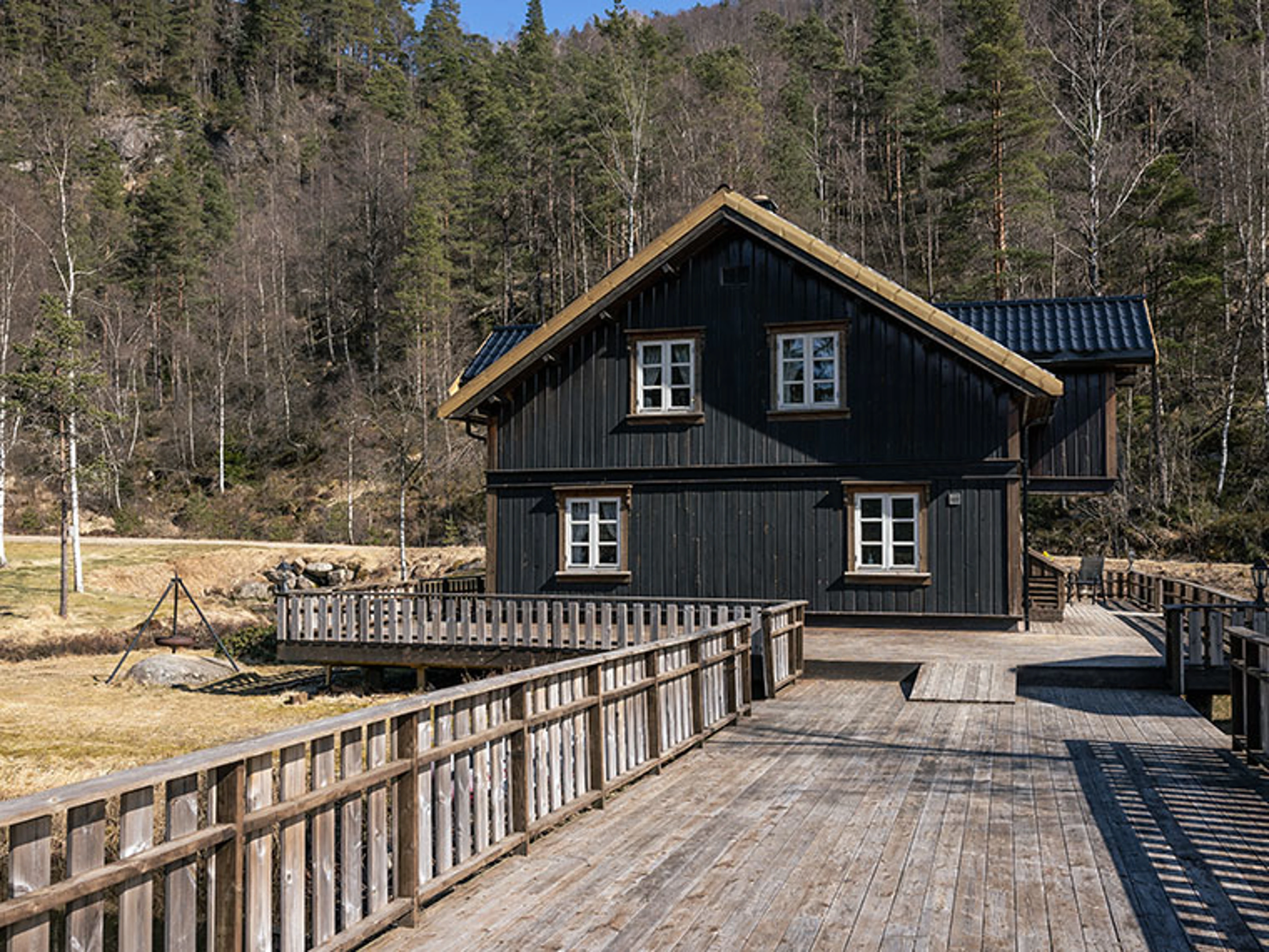 Sort træhus i naturen med skov bagved og badebro.